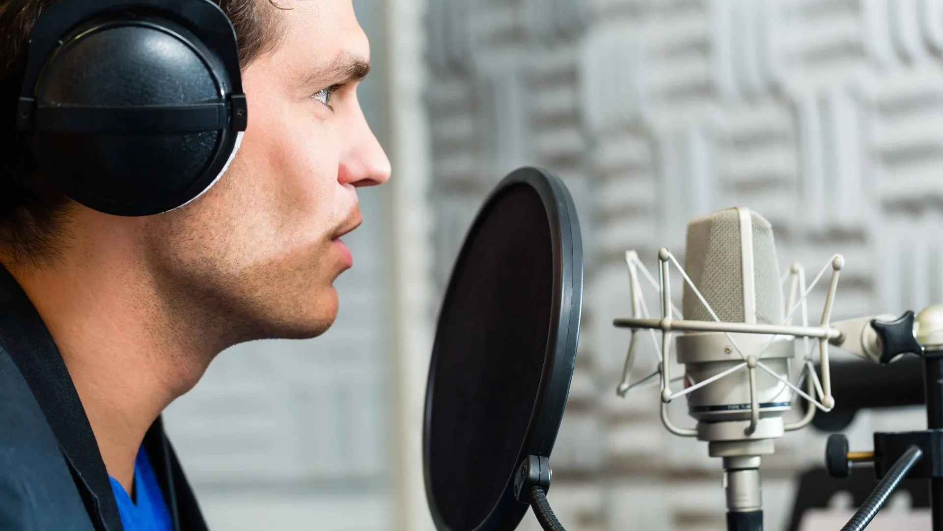 Voice talent in headphones speaking into a studio condenser mic behind a pop filter