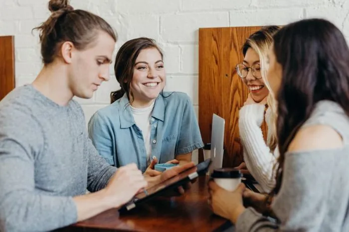 Vier junge Leute sitzen lachend am Cafétisch und schauen gemeinsam auf ein Tablet