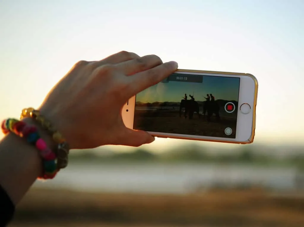 Hand films with a smartphone at dusk; the screen shows riders on elephants and a running record timer.