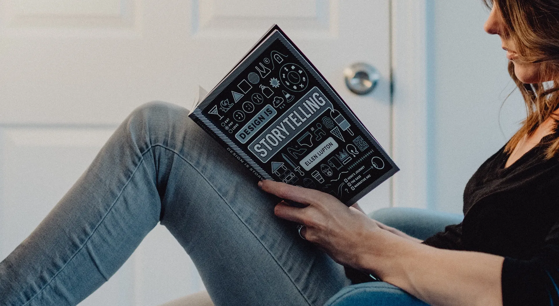 Woman sitting on a sofa reading the book “Design is Storytelling” by Ellen Lupton