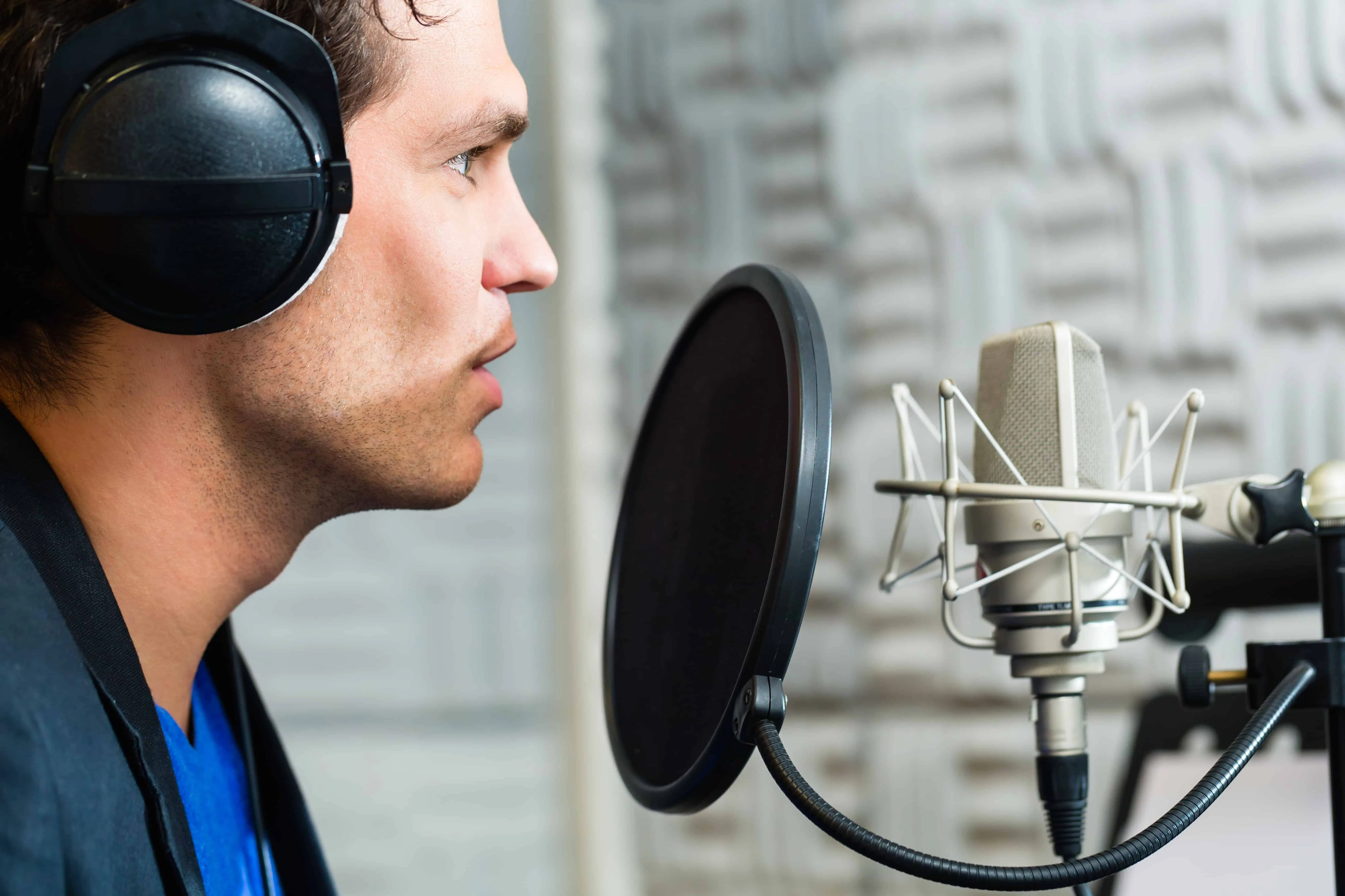Young male speaker or musician with microphone and headphone for audio recording in the Studio