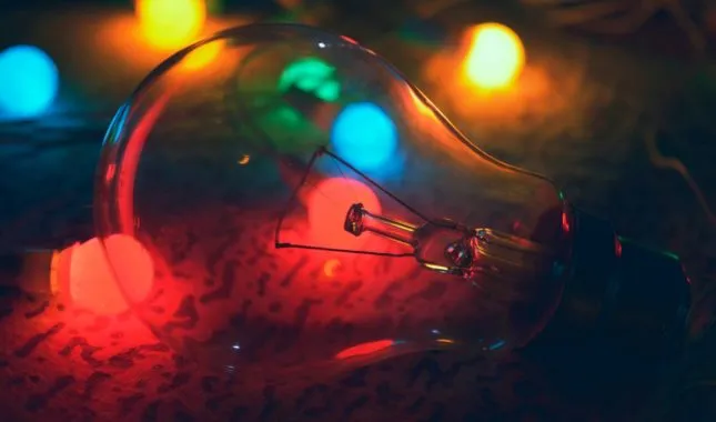 Clear light bulb lying among colourful fairy lights that glow red, blue and green around it