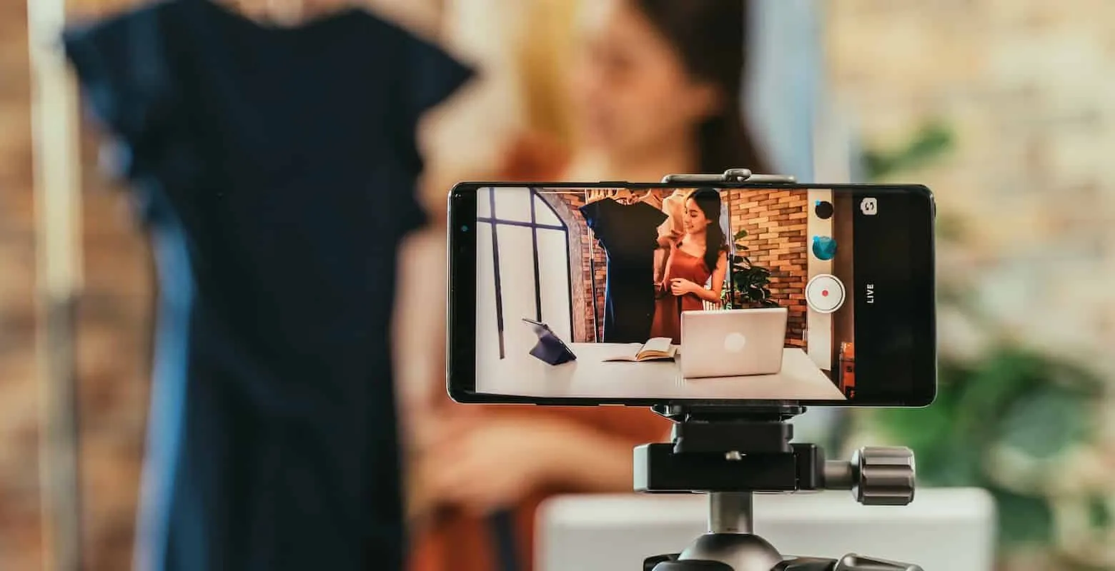 Smartphone on a tripod livestreaming a woman presenting clothes in a shop, LIVE on screen