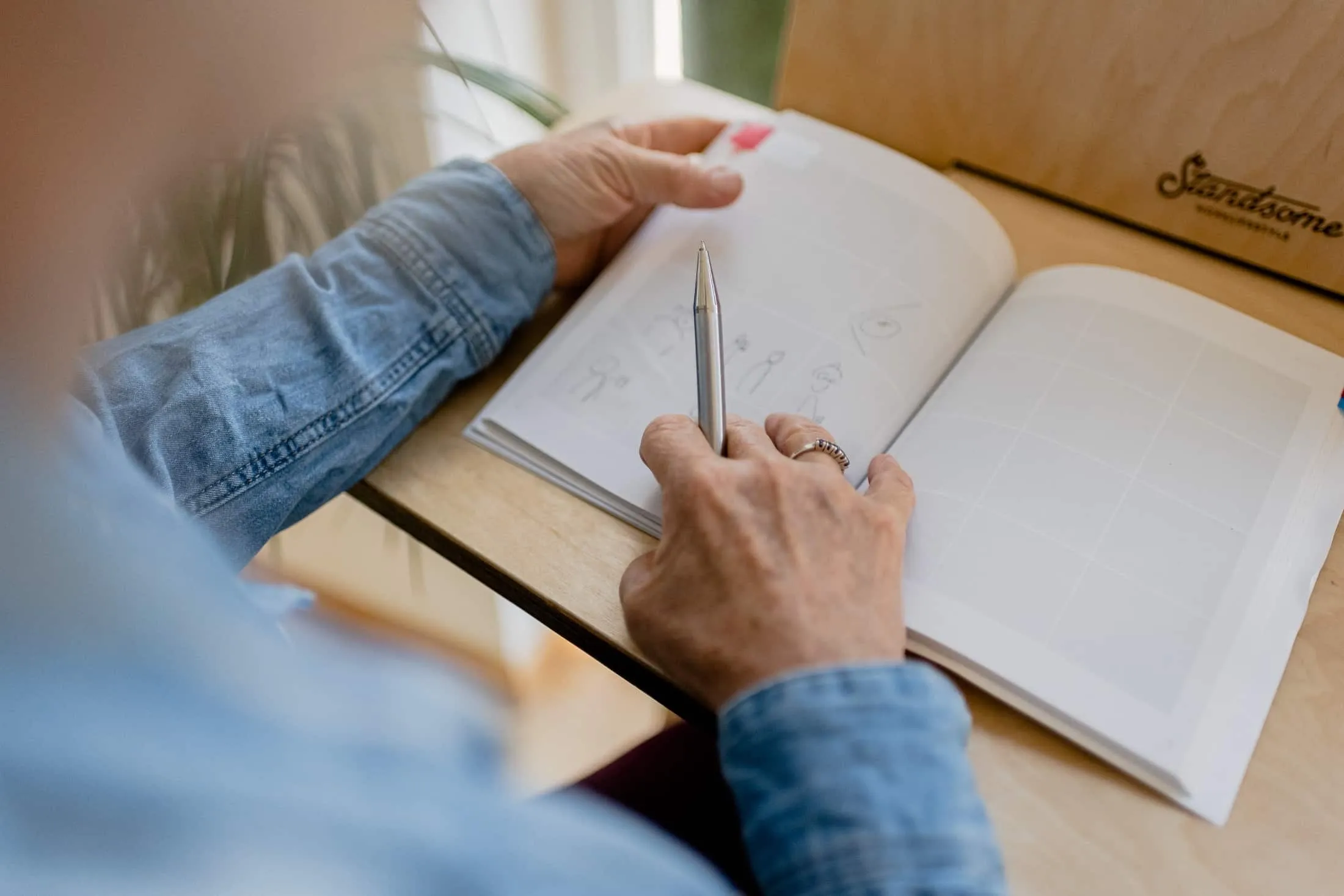 Someone sketches simple stick figures with a pen into the empty frames of a storyboard notebook.