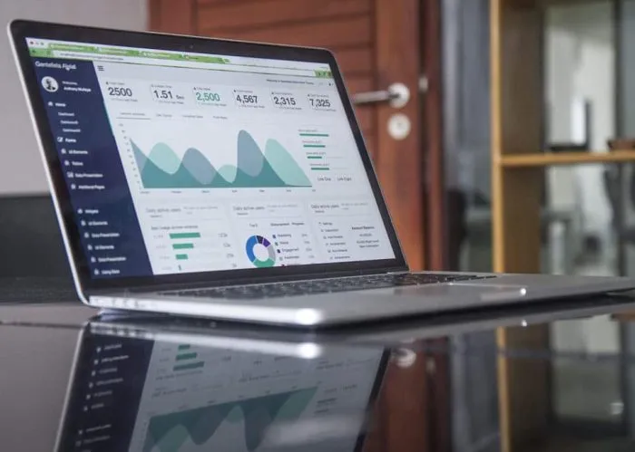 Laptop auf einem Glastisch zeigt ein Analytics-Dashboard mit Kennzahlen, Flächendiagramm und Donut-Chart