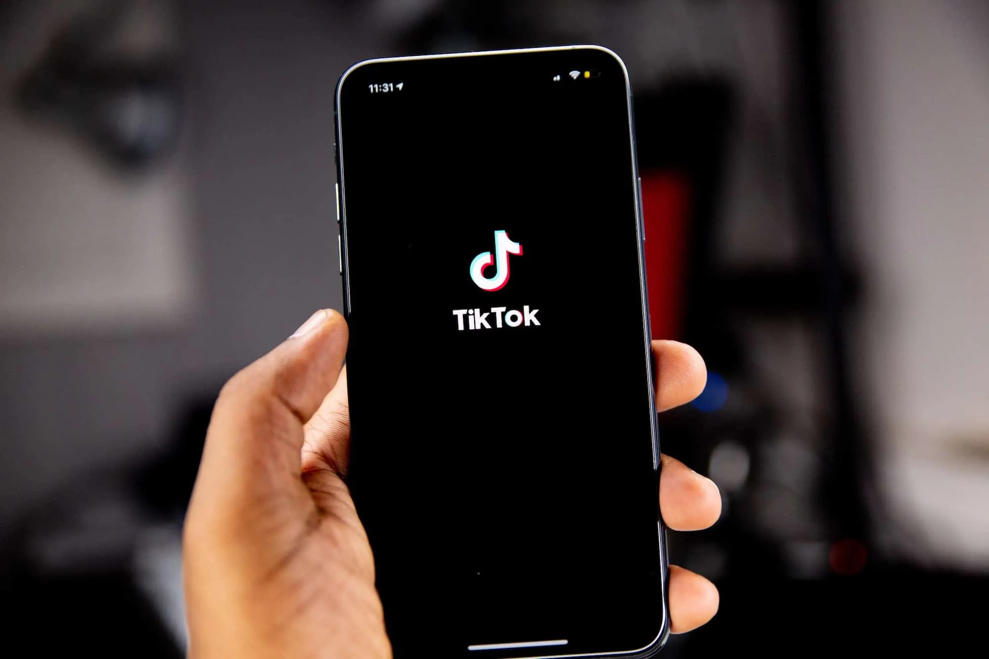 Hand holding a smartphone showing the TikTok splash screen with its logo.